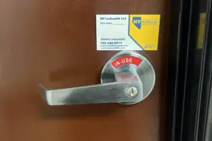 A metal door with a lever handle marked with a red IN-USE sign. Above the handle, a business card for NV Locksmith LLC is attached, showcasing contact details and highlighting their exceptional locksmith services in Las Vegas as a mobile locksmith.